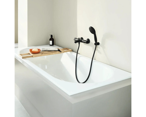 Moderne ligbad met badkraan en handdouche in een lichte badkamer, aangevuld met een houten badplank met accessoires.