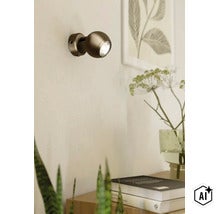 Moderne bolvormige wandlamp met LED lichtbron gemonteerd aan een lichte muur boven een plank met decoratie. (Image AI modified or generated)