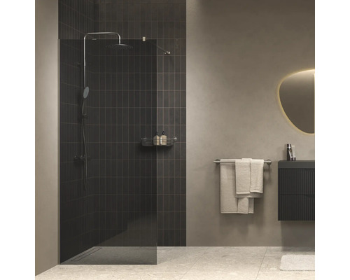 Moderne inloopdouche met glazen wand voor een donker betegelde muur, in een minimalistische badkamer met wastafelmeubel en spiegel.