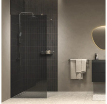 Moderne inloopdouche met glazen wand voor een donker betegelde muur, in een minimalistische badkamer met wastafelmeubel en spiegel.