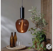 Moderne hanglamp met rookkleurig glazen armatuur en zichtbare gloeidraadlamp boven een houten tafel met decoratie. (Image AI modified or generated)