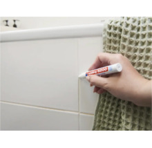 Persoon gebruikt een Edding 8200 voegenstift om de voegen van tegels aan een muur in een badkamer op te frissen.