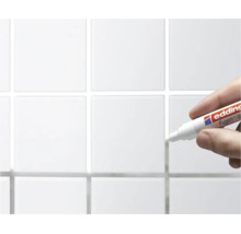 Hand houdt een Edding voegenstift vast voor het bijwerken van tegelvoegen op een betegelde wand.