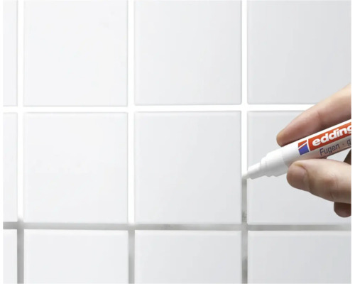Hand houdt een Edding voegenstift vast voor het bijwerken van tegelvoegen op een betegelde wand.