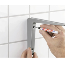 Iemand markeert de boorgaten voor een wandsteun op een betegelde muur met een Edding 8850 speciale marker.