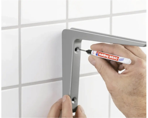 Iemand markeert de boorgaten voor een wandsteun op een betegelde muur met een Edding 8850 speciale marker.