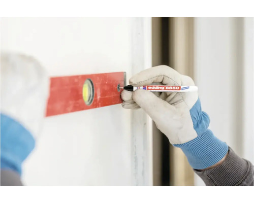 Hand in werkhandschoen markeert een boorgat met een Edding 8850 diepgatmarker door de opening van een waterpas op een muur.