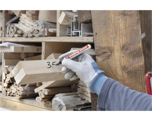 Persoon met werkhandschoen beschrijft houten balk met een Edding 3000 permanente marker in een houtmagazijn.