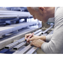 Ambachtman markeert een metalen profiel op een werkbank met een Edding 3000 permanente marker.