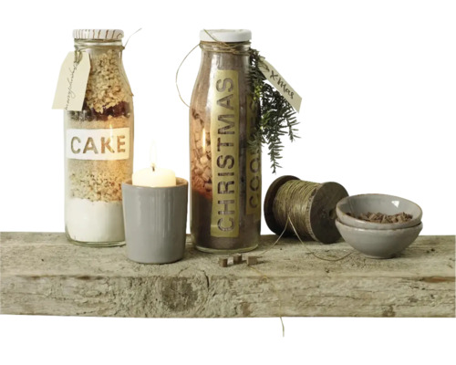 Twee glazen flessen met bakmixen, een kaars in een beker, een klos garen en twee kleine schaaltjes op een rustieke houten plank.