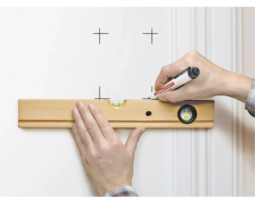 Een hand houdt een houten waterpas tegen een muur terwijl de andere hand markeringen tekent met een Edding marker.