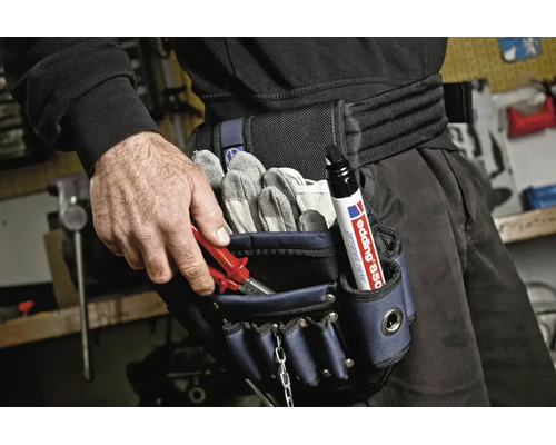 Vakman draagt een gereedschapstas met handschoenen, tang en een Edding permanente marker aan de riem in een werkplaats.
