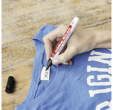 Een hand schrijft op het label van textiel met een Edding 8040 wasgoedmarker.