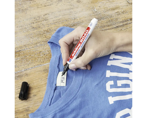 Een hand schrijft op het label van textiel met een Edding 8040 wasgoedmarker.