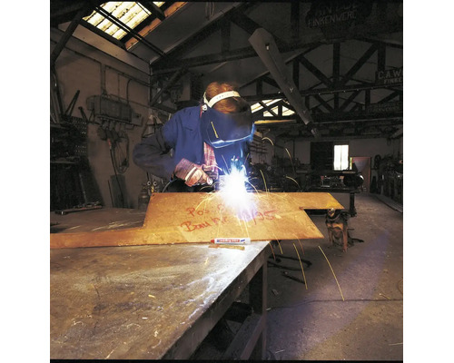 Een lasser bewerkt een metalen plaat met een Edding markeerstift in een industriële werkplaats.