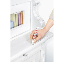 Een hand gebruikt een edding 8900 meubelstift om krassen op een licht houten meubelstuk bij te werken.