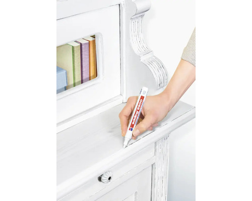 Een hand gebruikt een edding 8900 meubelstift om krassen op een licht houten meubelstuk bij te werken.