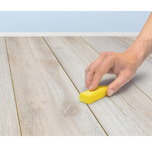 Een hand gebruikt een reparatiewasstift om krassen op een laminaatvloer te herstellen.