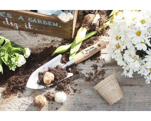 Gepersonaliseerde handtroffel van metaal met houten handvat en bloembollen op een houten tafel met plantenarrangement.