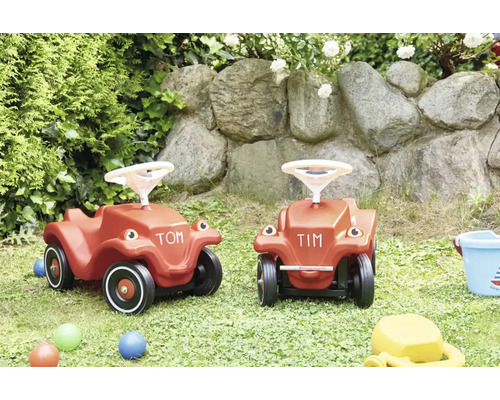 Twee kunststof loopauto voor kinderen in een tuin met natuurstenen muur.