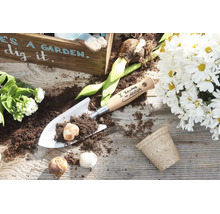 Gepersonaliseerde handtroffel van metaal met houten handvat en bloembollen op een houten tafel met plantenarrangement.