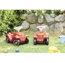 Twee kunststof loopauto voor kinderen in een tuin met natuurstenen muur.