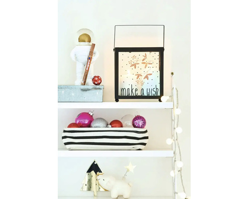 Kerstdecoratie op een plank met een lantaarn met tekst make a wish, kerstballen in een mand en kerstverlichting op witte planken.