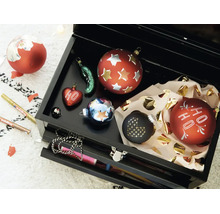 Een open zwarte gereedschapskist gevuld met verschillende kerstballen en twee Edding stiften voor decoratie.