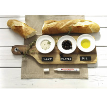 Een edding krijtmarker ligt op een houten plank met gelabelde schaaltjes voor zout, olijven en olie naast een stokbrood.