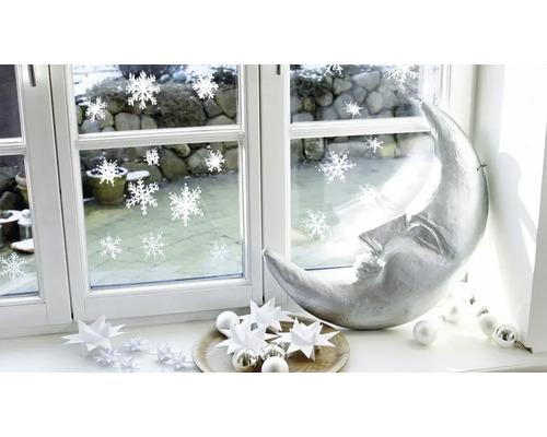 Kerstdecoratie op een vensterbank met een zilveren halve maan, papieren sterren en raamstickers met sneeuwvlokken.
