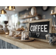 Een toonbank in een cafe met een krijtbord met de tekst Coffee en een kleine glazen stolp met gebak op de bar.