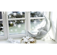 Kerstdecoratie op een vensterbank met een zilveren halve maan, papieren sterren en raamstickers met sneeuwvlokken.