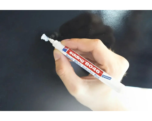 Een hand houdt een witte Edding 8046 industriële stift vast voor het markeren op een donker oppervlak.