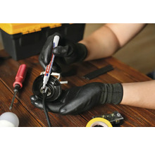 Een persoon met werkhandschoenen markeert een elektrisch onderdeel met een Edding lakmarker op een houten tafel.