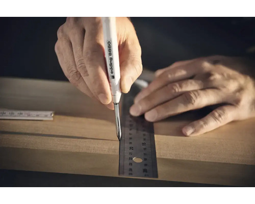 Een hand gebruikt een Edding 8880 diepgatmarker en een liniaal om een markering op een houten plank te maken.