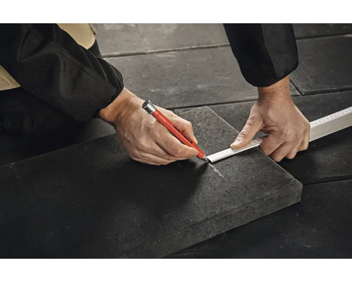 Handwerker tekent met een Edding markeringsstift een lijn op een donkere steenplaat met behulp van een duimstok.