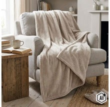 Een zachte woondeken ligt decoratief over een gestoffeerde fauteuil in een gezellig ingerichte woonkamer. (Image AI modified or generated)
