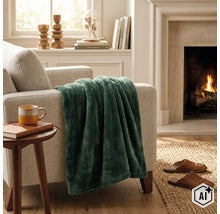 Een zachte woondeken op een fauteuil in een gezellige woonkamer met open haard. (Image AI modified or generated)
