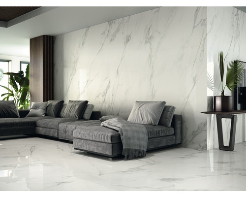 Lichte woonkamer met grijze bank, kamerplanten en wand- en vloertegels in marmerlook.