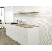 Keukenscène met witte onderkasten, een houten plank en een muur met een golvende tegelstructuur.