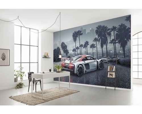 Woonkamer met fotobehang, dat een auto voor een skyline met palmbomen toont, plus bureau, stoel en decoratie.