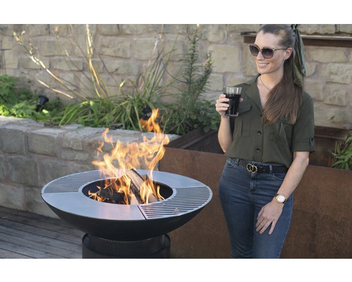 Vuurplaats met hout en een vrouw met een drankje in de tuin