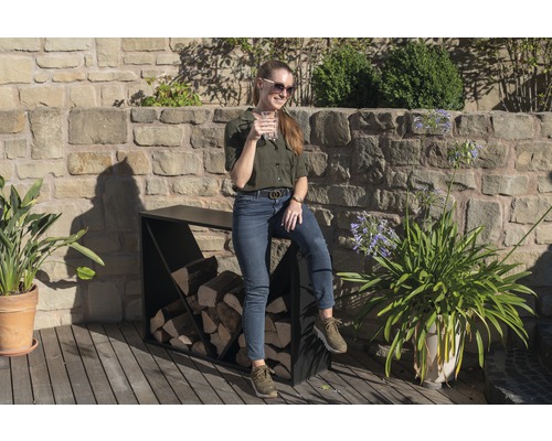 Vrouw zit op een brandhoutrek buiten met metselwerk op de achtergrond.