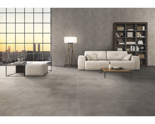 Woonkamer met grijze vloertegels, bank, boekenkast en groot raam