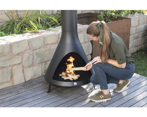 Vrouw legt hout in een zwarte tuinhaard