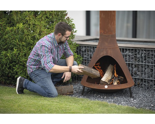 Man legt hout in een roestkleurige tuinhaard.