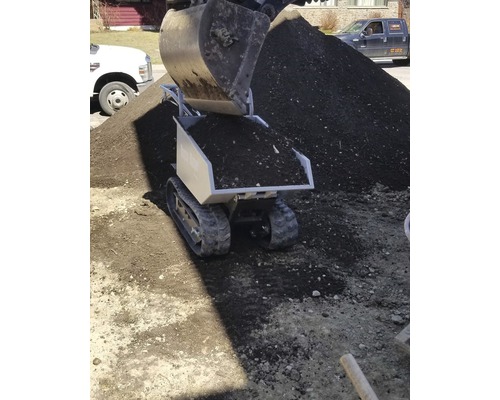 Mini-dumper met rupsbanden en aarde wordt gevuld door graafmachine