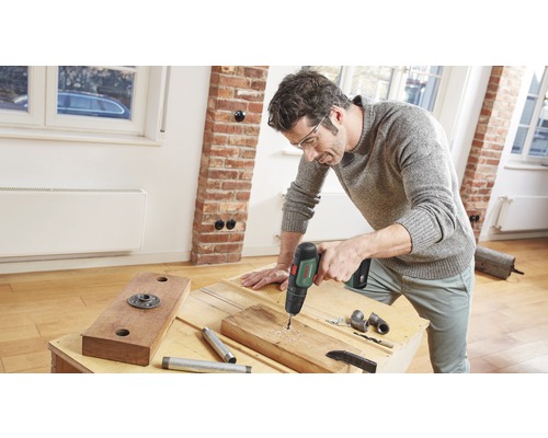 Een man boort een gat in een houten plank met een boormachine.