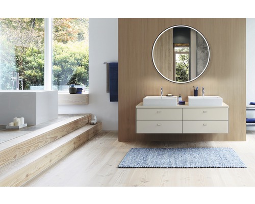 Badkamer met dubbele wastafel, spiegel met verlichting en ligbad op een verhoogd niveau