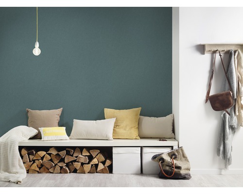 Woonkamer met groene muur, zitbank, kussens, houtblokken, opbergdozen en kapstok